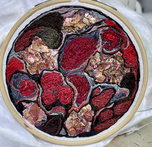 Circular embroidery in shades of red, brown, and gray. Orange-pink ares made of broken eggshells.