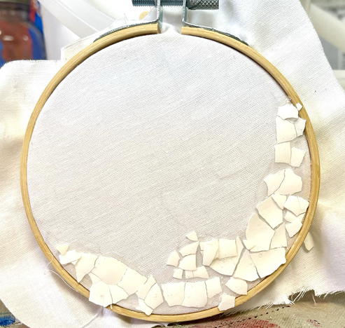 Circular embroidery cloth with broken eggshells along the bottom-right edge