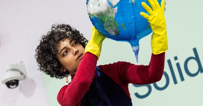 A woman wearing yellow gloves holding a balloon that looks like planet heart