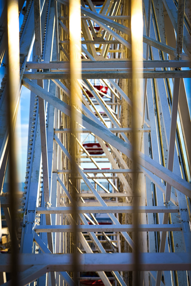 A view of empty Ferris wheel cars shot from another Ferris wheel car. Strong white vertical bars cut through the foreground of the image with bits of the cars red and white polka dots sticking through form the bottom and background. 
