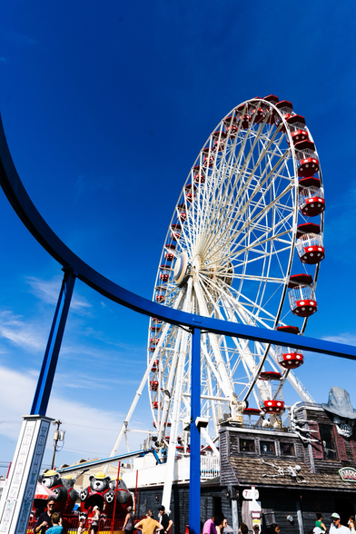 A big white and red Ferris wheel shot from the ground a curving blue monorail track bisects the the imagine. Both shot against a deep blue sky. 