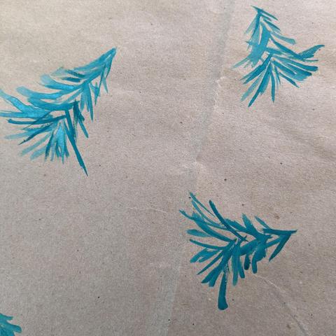 Alt text: Image displays brown paper bag laid flat with evergreen trees painted on it, decorated as Christmas gift wrap.