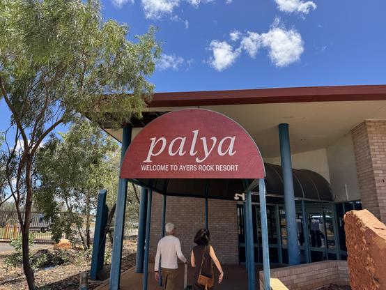 Entry way on the tarmac at Ayers Rock Connellan airport. The entrance is a red arch, probably a symbol of the Uluru, saying "palaya" in big letters and "Welcome to Ayers Rock Resort" underneath.
