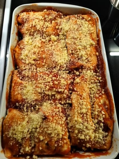 Enchilladas ready to go into the oven are covered with shreadded cheese and tomato sauce 