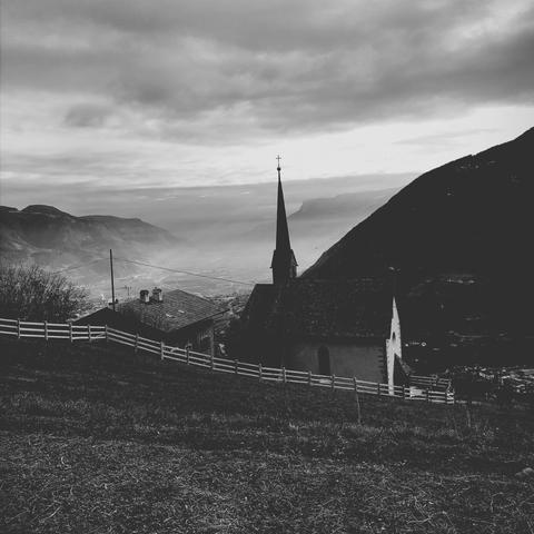 Una chiesetta in montagna su di un grande prato e la pianura sottostante