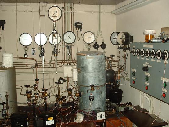 Ein komplizierter Aufbau aus 2 Behältern , einen Kühlschrank Kompressor, einer Schaltschrank mit einer reihe von Knebelschaltern und Tastern . An der Wand befeinden sich noch verschiedene Manometer . Und das alles ist mit dünnen Kupferrohren verbunden.  