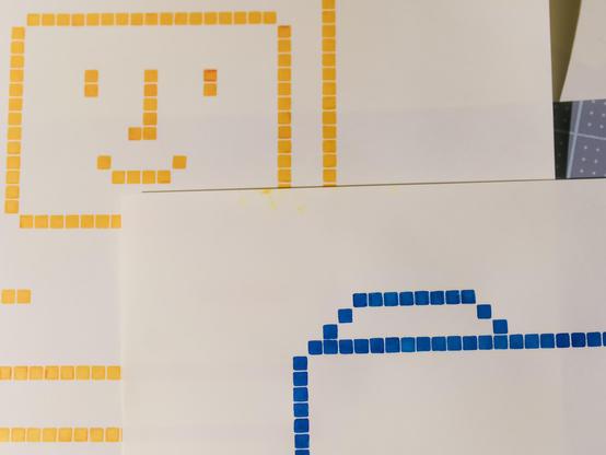 Fountain pen illustrations of the Happy Mac and Folder icons, in yellow and blue respectively. The drawing emulates the pixellated design with numerous defined squares.