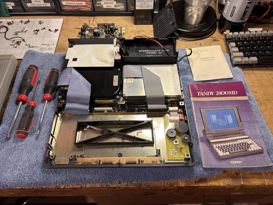 A disassembled Tandy 2800 HD laptop showing internal hard disk, floppy drive, power supply, and battery compartment.