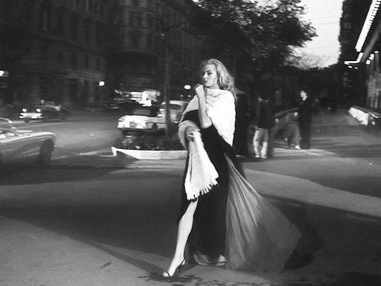 a woman with long blonde hair and a stylish dress walking through the street