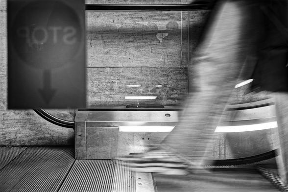 Une photo du bas d'un escalator avec une jambe entamant le dernier pas.