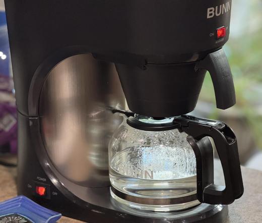 A black coffee maker with a glass carafe is shown, filled partially with freshly brewed water.  This is the result of not being very awake and missing the step to add the coffee after grinding it. 