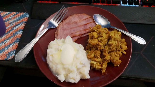 Ham, Mashed Potatos, & Stuffing on a red glass plate with a Fork and Spoon laying around the plate.