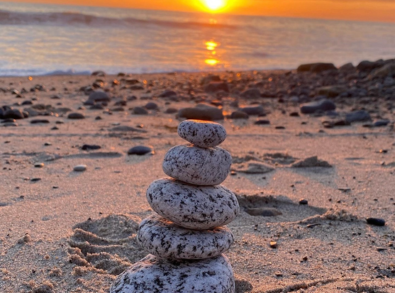 Stack of black and white rocks on a beach with the sun setting over the ocean in the background. Photo by Jennifer Rogers 
