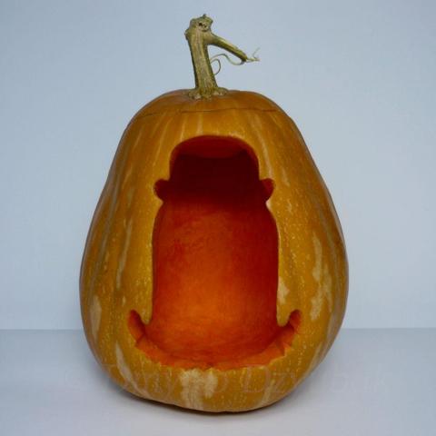 Cousin Itt from The Addams Family, diminutive, floor-length hair being, wearing a bowler hat is depicted on a carved pumpkin.