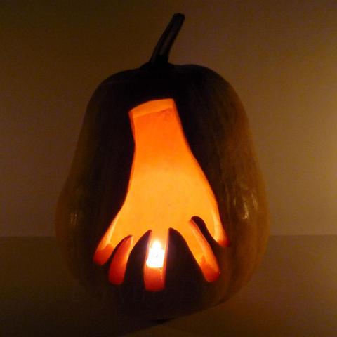 Thing T. Thing from The Addams Family, disembodied hand, running on his fingertips is depicted on a carved pumpkin. Pumpkin with a tealight candle inside at night.