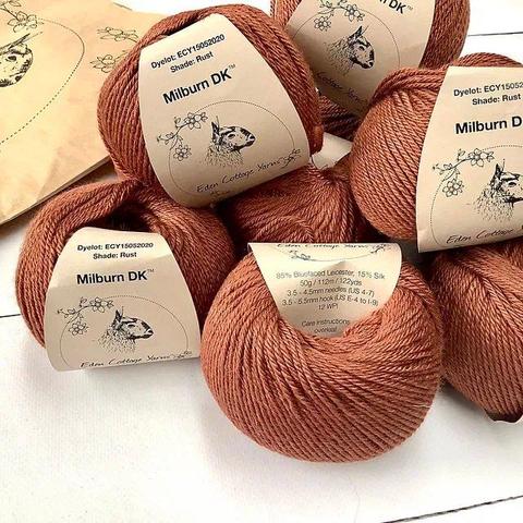 A pile of rust colored yarn with brown labels on a white plank background.