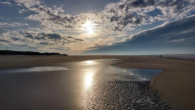 Sonne und Wolken über der Nordsee die sich im Watt spiegeln.