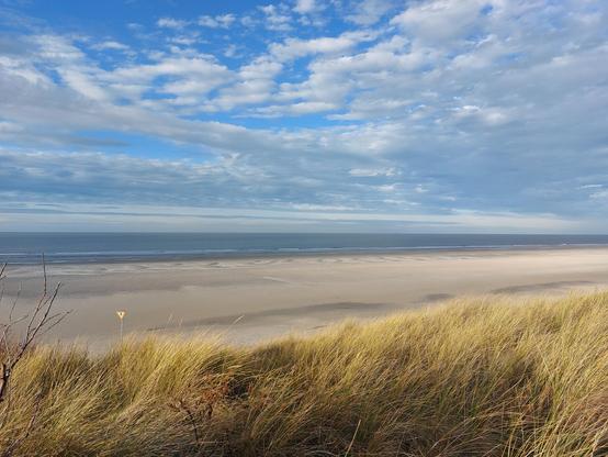 Ausblick von einer Düne über den Strand zur Nordsee. Blauer Himmel teilweise bewölkt