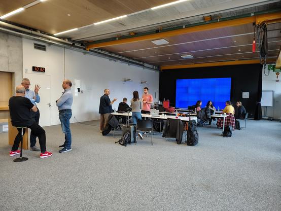 Several people discussing in a workshop manner in a large meeting room at the University of the Grisons during the 2024 EDDI conference.