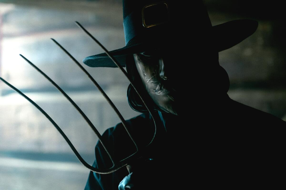 The John Caver villain from the 2023 horror movie, Thanksgiving. He is wearing the John Caver mask, pilgrim hat, and is holding a pitchfork.