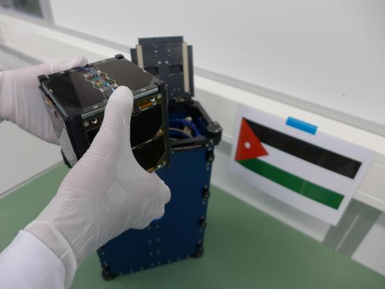 JY1sat CubeSat held with white gloves, about to be inserted into a QuadPack launch canister. 