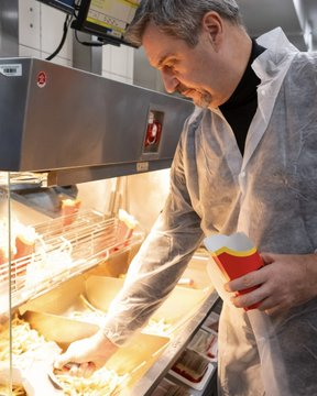 Markus Söder bei einem PR-Besuch bei McDonalds. Er füllt ebenfalls Pommes ab.