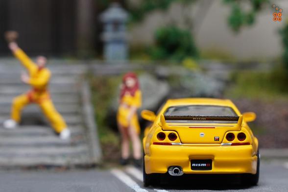 A rear side of Nissan Skyline GT-R (R33) Nismo 400R Yellow by Pop Race in 1:64 scale with 1:64 figures on AREA 164