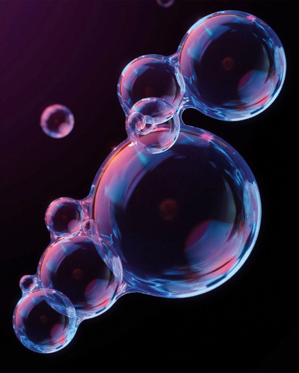 
A cluster of translucent soap bubbles floats against a dark background, illuminated with soft pink and blue light. The bubbles' surfaces shimmer with reflections, creating a dreamy and abstract