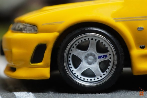 A close-up shot of Nissan Skyline GT-R (R33) Nismo 400R Yellow by Pop Race in 1:64 scale with 1:64 figures on AREA 164