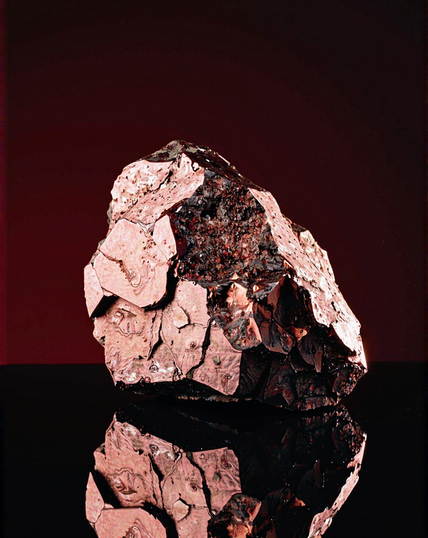 A textured rock with rose-gold hues, shimmering under soft light and reflecting on a glossy black surface, evoking an impression of natural elegance and timeless beauty.