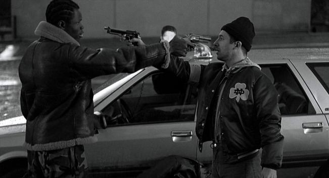 Two men are the central focus. One, a Black man with short braids, is wearing a leather jacket and camouflage pants. He's holding a handgun pointed at the other man. The second man, who appears to be white, is wearing a black beanie and a varsity jacket. He's also holding a handgun, pointed at the other man. Their faces show intensity and a grim determination.
