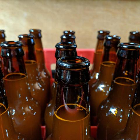 A closeup photo of beer bottles after they have been filled with beer but before they have been capped. The bottles are brown, the beer looks cloudy because it is. They are sitting in a red plastic bottle crate that holds 24 bottles.