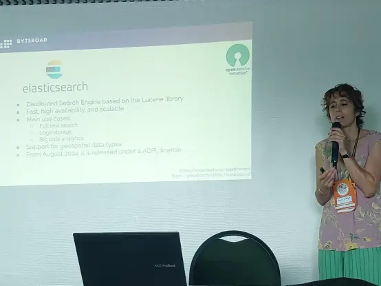 Joana Simões talking next to a conference screen.