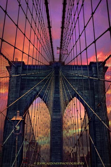 Dramatic lines of cable and steel converge towards the center of the iconic Brooklyn Bridge against a stunning sunset sky. Rich hues of pink, purple, and orange create a vibrant backdrop that highlights the architectural details.