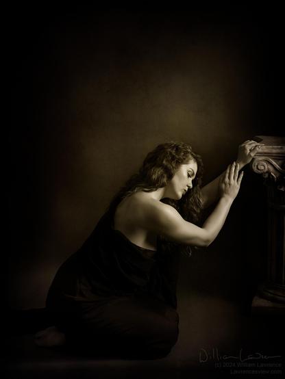 Toned black and white photo of model Jessa Ray Muse, torso wrapped in black fabric kneeling in front of a pillar.  A very low-key scene (greys on blacks with orange and blue tones to add an air of somberness).