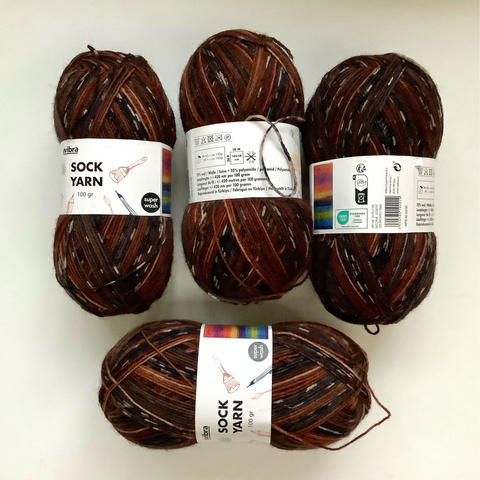 4 balls of variegated yarn in browns and black on a white background.
