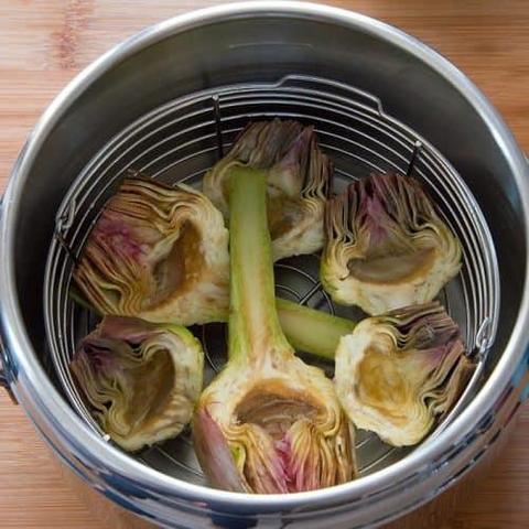 An image of 3 artichokes that were halved, steamed and cooked to perfection with the inner portion of them facing upward. They were placed on top of a steaming tray and inside a cooking pot for the cooking process.
