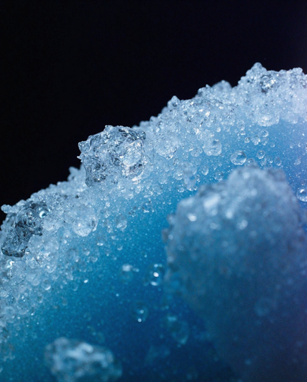 A close-up of sparkling ice crystals clinging to a textured blue surface, with glistening highlights capturing the frosty beauty of winter.