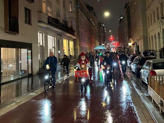 Radfahrende auf rot asphaltiere Fahrbahn zur Kennzeichnung als Fahrradstraße, im Vordergrund ein als Sinterklaas verkleideter Mann