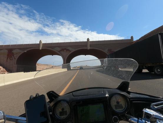 POV of  motorcyclist riding under  a modern stone bridge with two arches. In the right lane is a large truck.