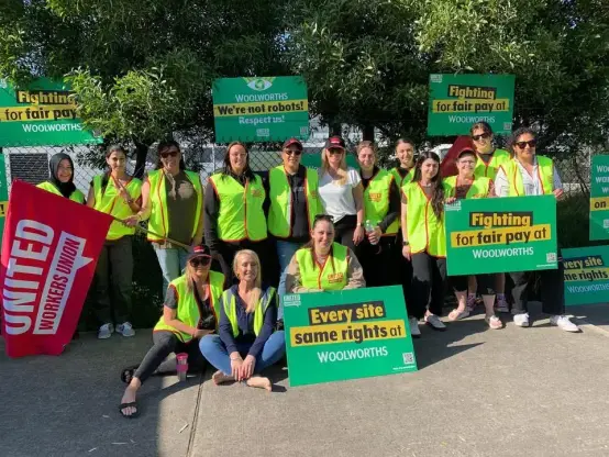 UWU warehouse workers wearing “high-viz” safety vests 
On their picket line outside Woolworths Warehouse 
Holding UNITED Workers Union Flag, 
UWU signs: 
Every Site Same Rights 
Fighting for Fair Pay 
We’re not Robots.
