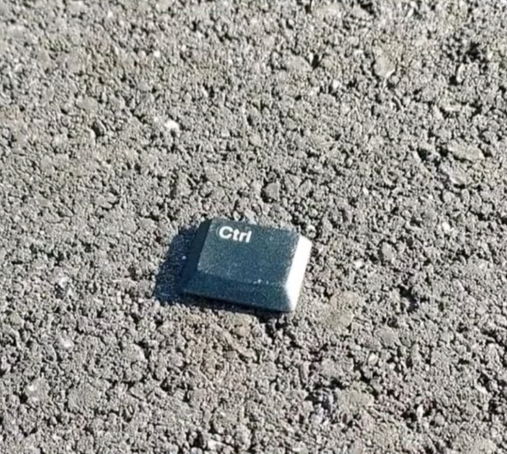 The image shows a single "Ctrl" key from a keyboard lying on a rough, textured surface, likely asphalt or concrete. The key appears to be detached from its keyboard and is positioned at an angle. 