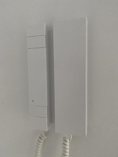 A picture of a white, geometric intercom, with a rectangular handset and integrated buttons, where form is prevalent over function.