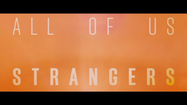 The words "ALL OF US STRANGERS" are displayed in a sans-serif font against a blurry orange background. 