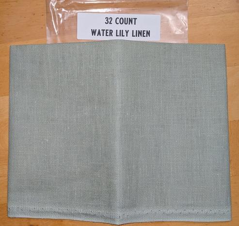 A piece of light sage greenish linen fabric. The label behind it states 32ct water lily linen.