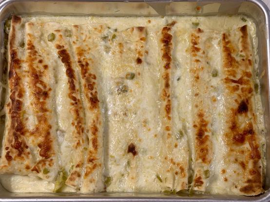 A baking dish full of chicken enchiladas with white cream sauce and toasted Monterey Jack cheese on top.