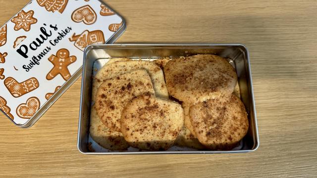 A tin labeled "Paul's Swiftmas Cookies" contains several cinnamon-sugar topped cookies, resting on a wooden surface.