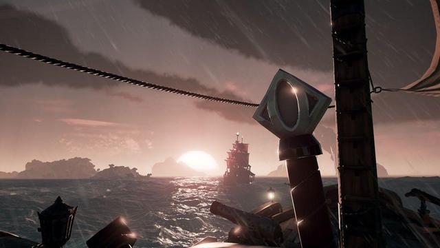 A screenshot form the game Sea of Theives. A large ship with red sails is in the background, framed by a sunrise and nearby islands. In the foreground is a single sail, a a ship's deck with cannons, unlit lanterns, and a ship's wheel. Rain is falling.
