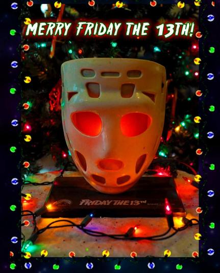 A hockey mask, illuminated by colorful lights, sits in front of a Christmas tree, on a mat printed with the words "Friday the 13th"
The caption reads, "Merry Friday the 13th"