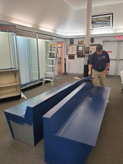 A staff member at Albacore Park paints two large benches. Once grey, they are now navy blue. 